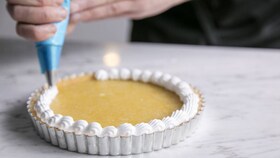 A baker piping the smooth meringue mixture onto the lemon meringue pie